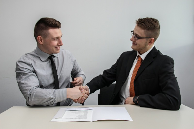 two people shaking hands over paperwork at a desk
